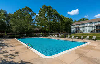 A large swimming pool surrounded by trees and chairs.