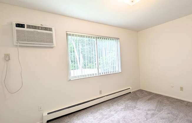 A room with a window, air conditioner, and carpeted floor.
