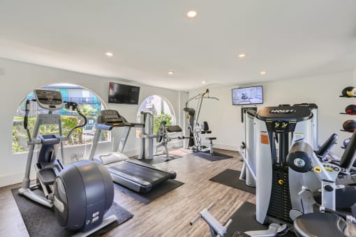 a gym with various machines and televisions on the wall