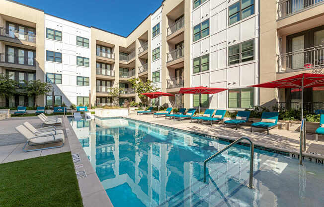 A swimming pool with lounge chairs and umbrellas in front of apartment buildings.