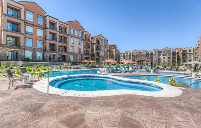 a swimming pool with lounge chairs and umbrellas in front of an apartment building