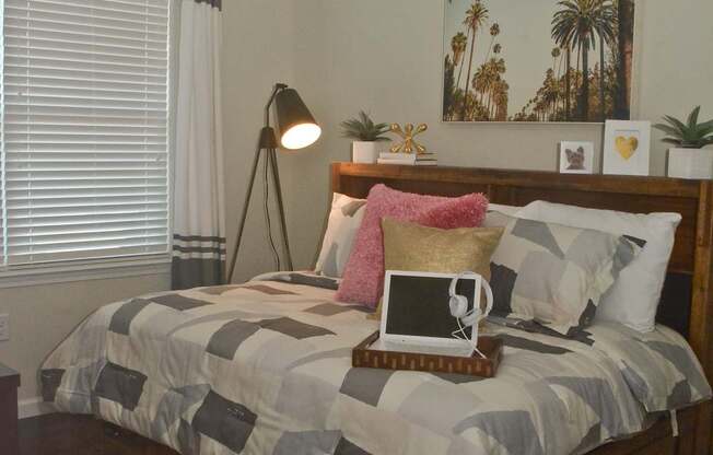 A bed with a grey and white comforter and a pink pillow on it.