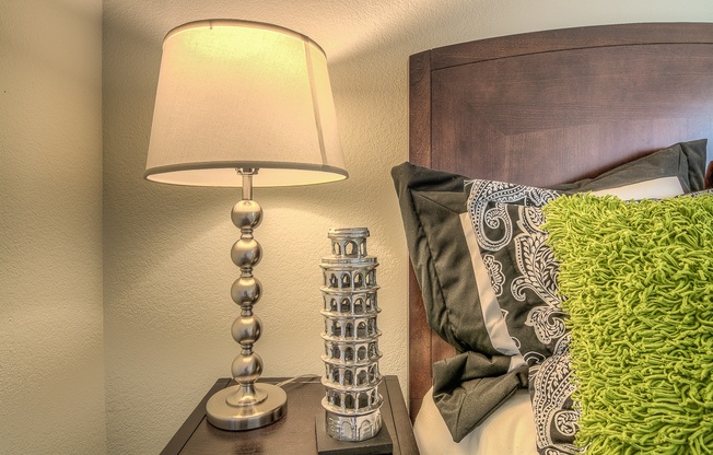 A lamp with a base of silver balls is on a bedside table next to a green pillow.