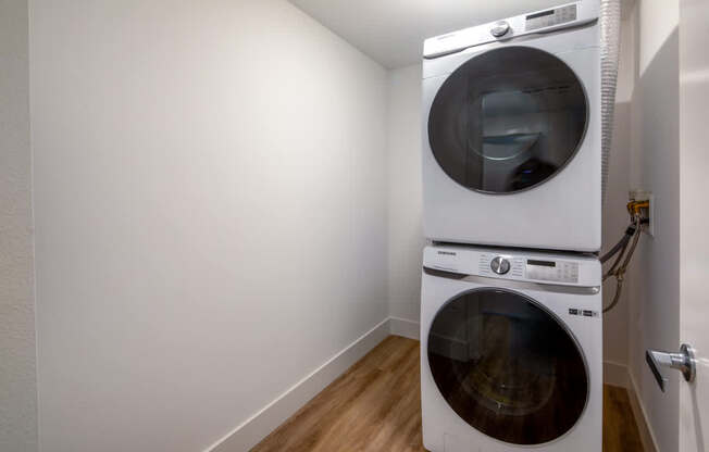 A white dryer is on top of a white washing machine in a small laundry room.