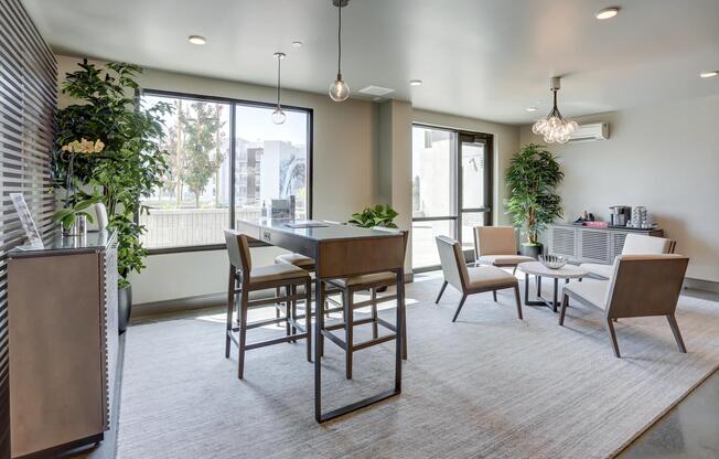 Light‑filled coworking area with a high‑top table, relaxed seating, and greenery throughout the room.