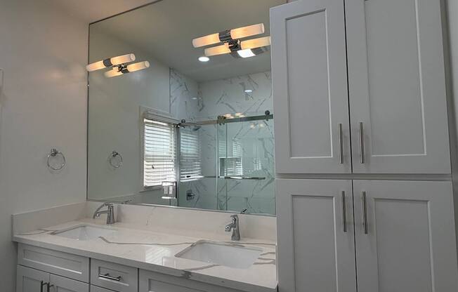 A bathroom with a large mirror, two sinks, and white cabinets.