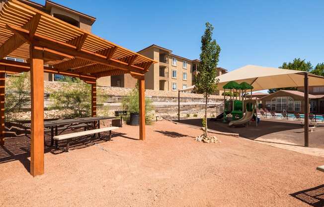 A wooden pergola is in the foreground of a sandy area with a building in the background at West Park Apartments, Albuquerque, New Mexico