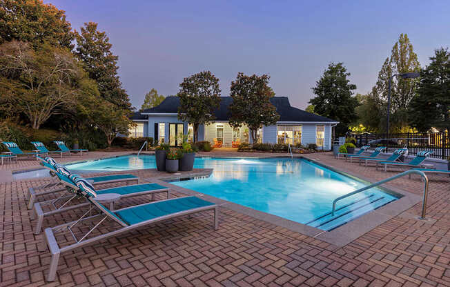 A pool with lounge chairs and a house in the background.