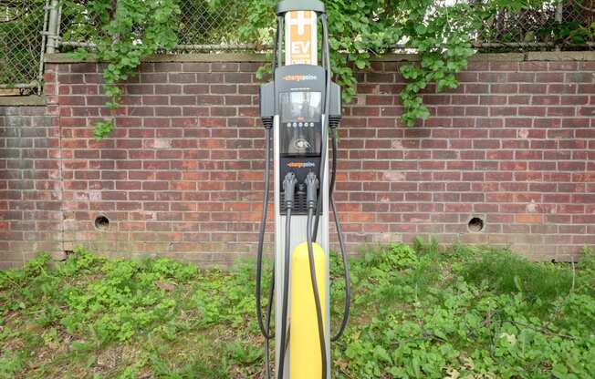 A yellow and black electric vehicle charging station sits in front of a brick wall.