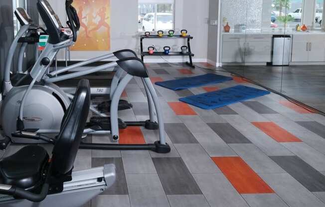 Fifteen 50 apartments near Las Vegas strip on site fitness center with modern orange and grey tile floor and exercise equipment facing wall TVs.