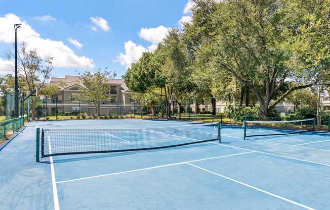 A tennis court surrounded by trees and a building in the background.