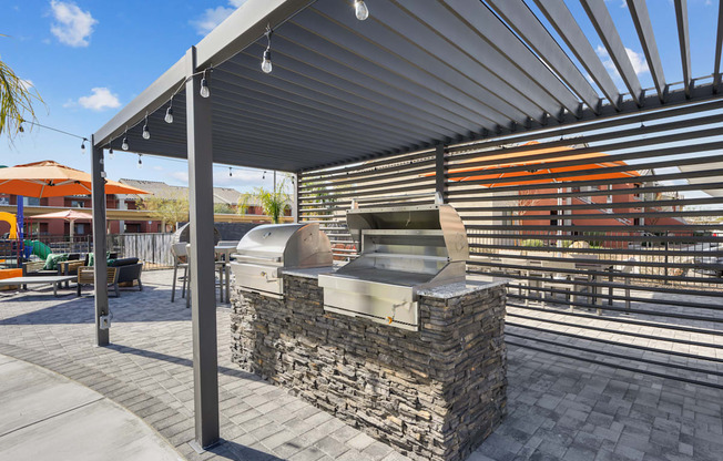 A stone grill is on a patio under a metal roof.