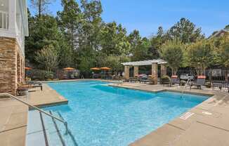 A large swimming pool surrounded by trees and a covered seating area.
