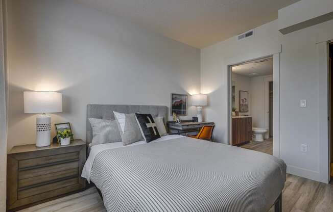 Bedroom with open door into en-suite bathroom, wood-tone floors, and décor