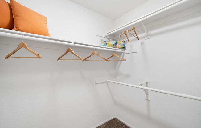 a spacious closet with white walls and white hangers with orange pillows on top