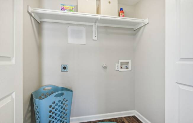 a small laundry room with a blue laundry basket and a shelf