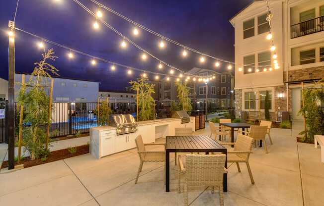 Two Gas BBQ's and outdoor seating area at nighttime. White lights are strung back and forth across that light up the area at Morgan Ranch Apartments, California, 95037