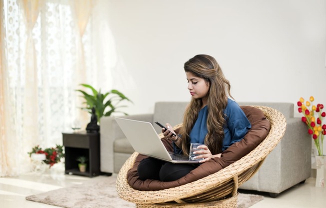 young woman sitting in a bean bag chair using her laptop and texting on her phone