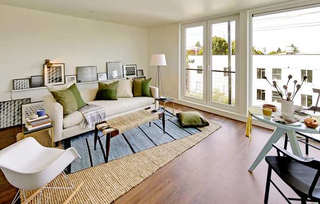 Living room with floor to ceiling windows with city and tree views. Staged with a couch, coffee table, rug and chair.at 19th & Mercer, Seattle Washington