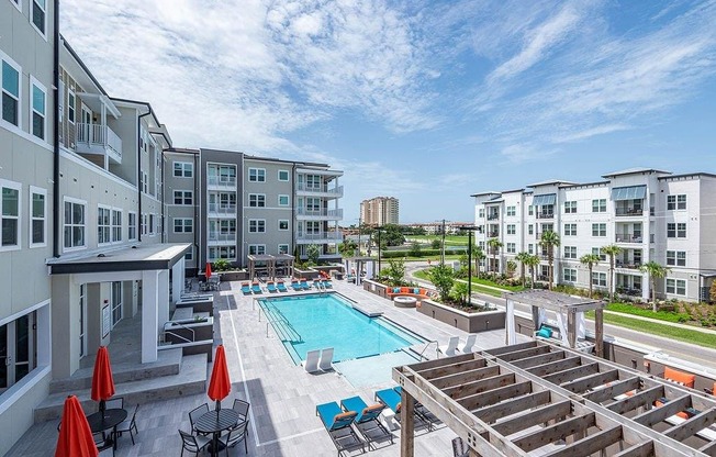 a swimming pool with lounge chairs and umbrellas in front of an apartment building