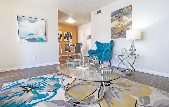 A living room with a glass coffee table and a blue chair at The Drake in Bossier City, LA