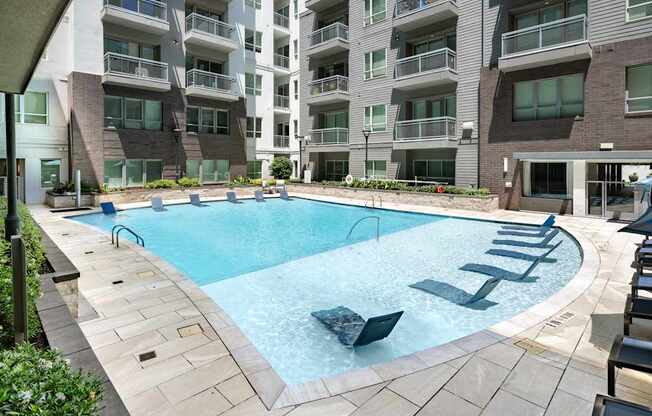 A large outdoor swimming pool surrounded by lounge chairs and buildings.