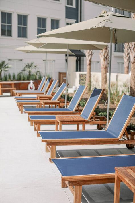 a row of lounge chairs with umbrellas in front of the soothing pool at The Merchant Apartments, Charleston