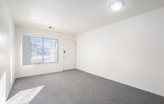 A room with a carpeted floor, a window, and a door.