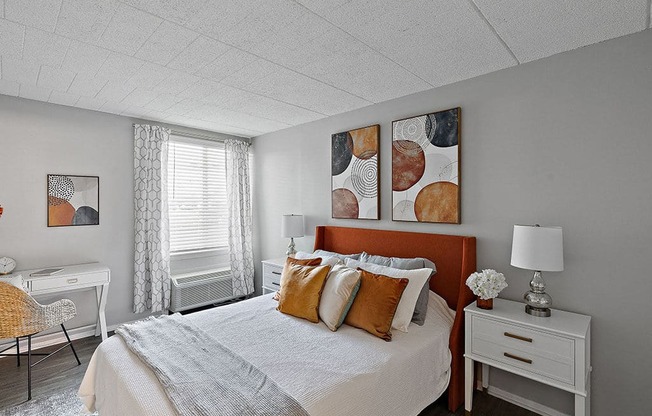 A bedroom with a bed, desk, chair, and two paintings on the wall.