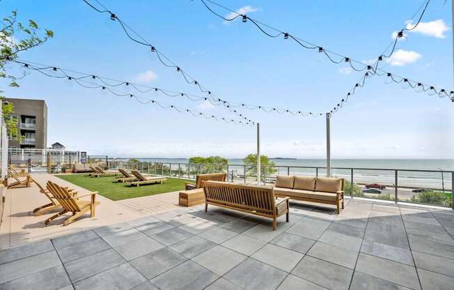 A patio with wooden furniture and string lights overlooking the ocean.