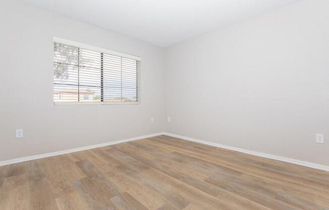 A room with wooden flooring and a window with blinds.