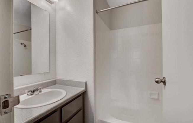 A white bathroom with a sink and a shower.