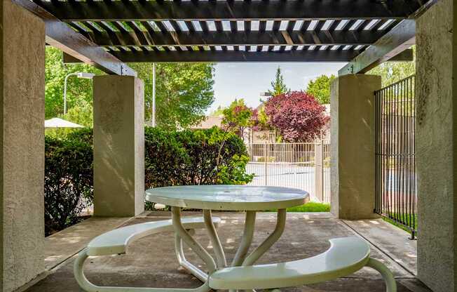A white table and two chairs are under a metal roof.