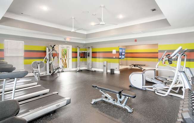 a gym with cardio equipment and weights in a building with yellow and orange walls at Avalon Apartment Homes, Starkville, MS, 39759
