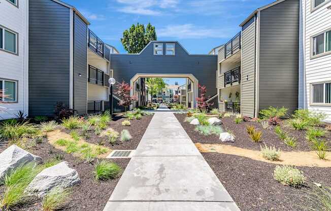 A concrete pathway leads through a landscaped courtyard between two buildings.