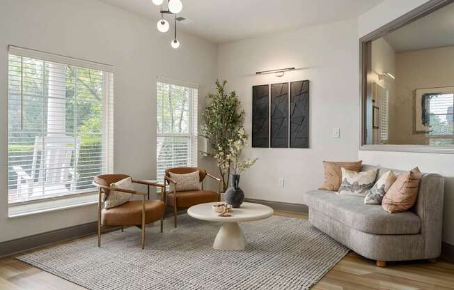 A living room with a grey couch, a wooden chair, a round table, and a potted plant.