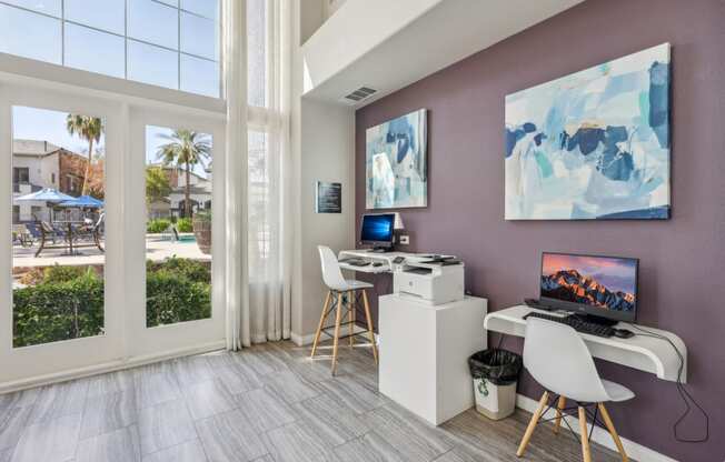 a room with a desk with a computer and chairs and a window