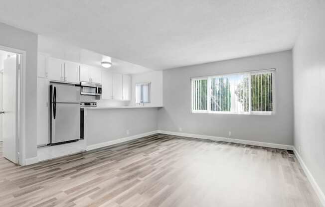 the living room and kitchen of an empty apartment with wood flooring and a window