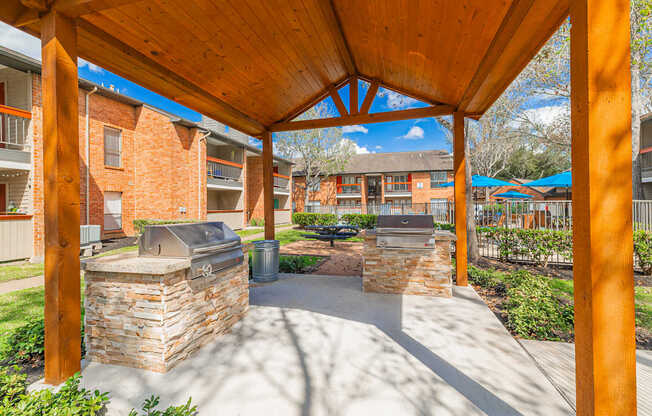 A wooden pergola with a stone fireplace underneath it.