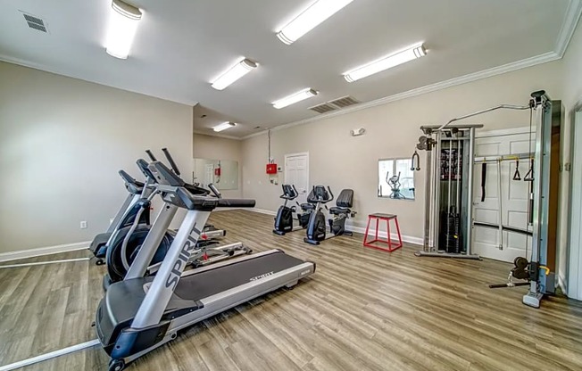 a gym with cardio equipment and weights on a wooden floor