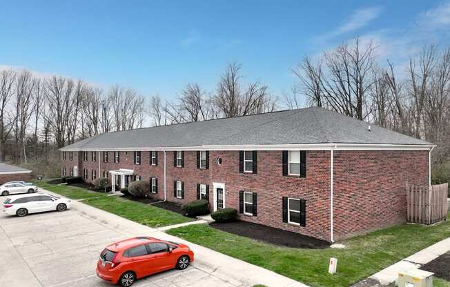 A red car is parked in a parking lot in front of a brick building.