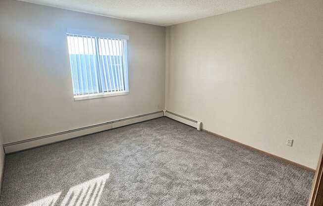 A room with a carpeted floor and a window with blinds.