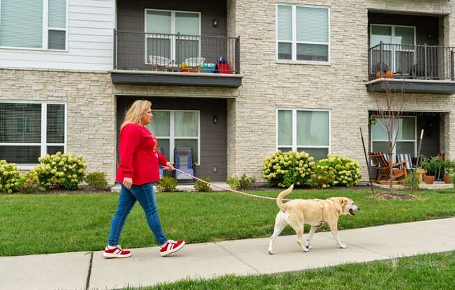 A woman walking her dog in front of a building.