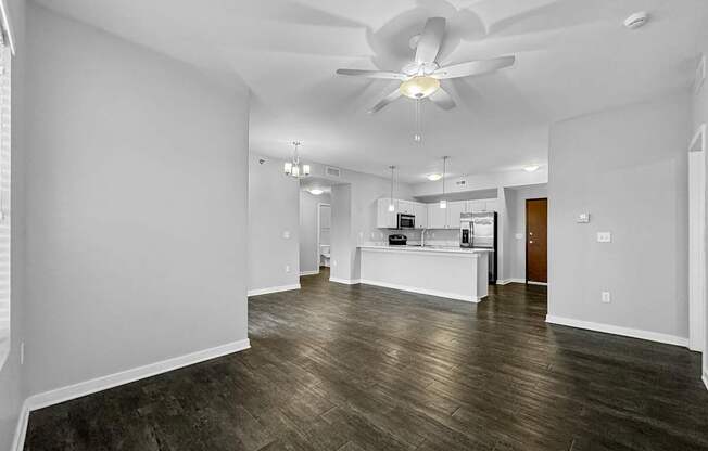 an empty living room with a ceiling fan and a kitchen