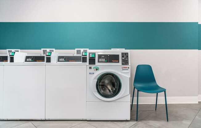 a row of washing machines in a laundry room with a blue chair