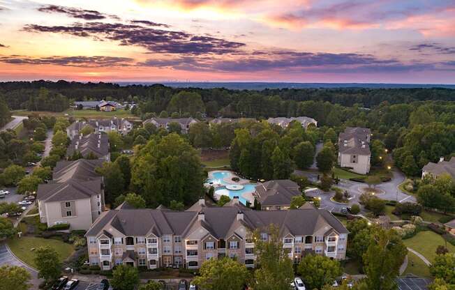 An aerial view of a residential area with houses and a pool during sunset.