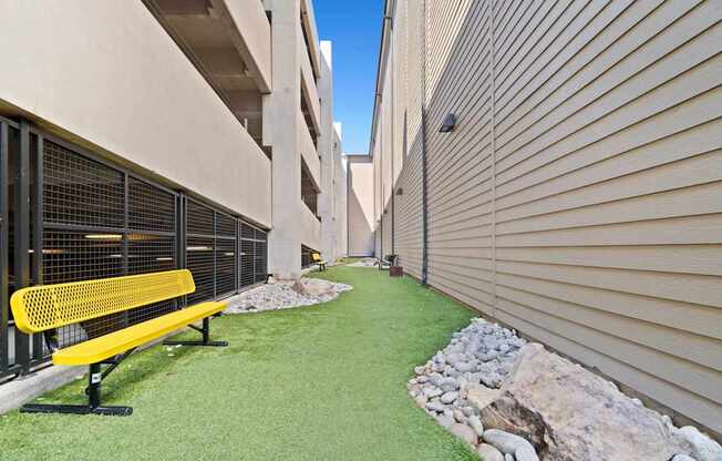 A yellow bench sits on a green lawn in front of a building.