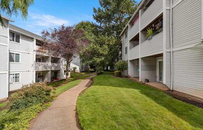A pathway leads through a grassy area between two apartment buildings at Clackamas Trails Apartments, Oregon, 97222
