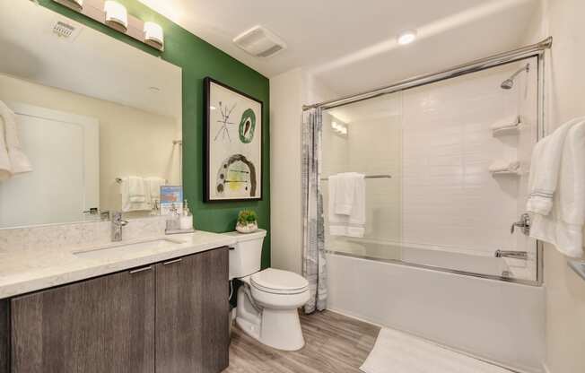 Bathroom with green accent wall. White tub/shower combination with sliding shower doors and hardwood inspired flooring at Morgan Ranch Apartments, Morgan Hill, California