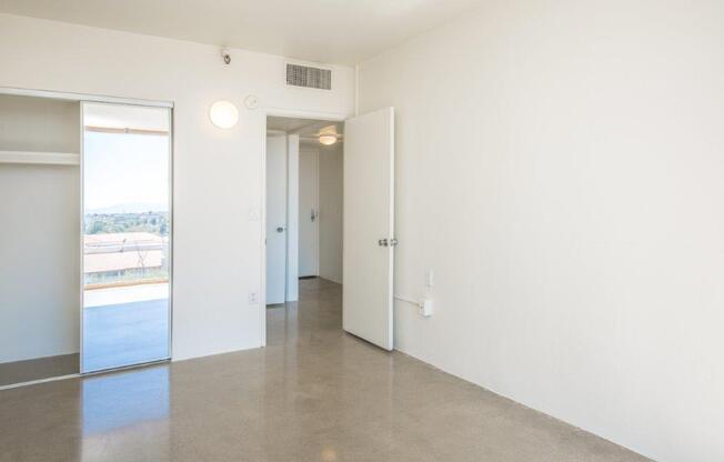 A large, empty room with a sliding glass door and a white door.